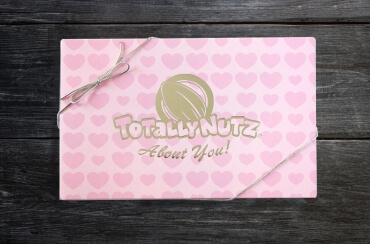 light pink box with darker pink hearts wrapped in a gold ribbon with gold Totally Nutz logo which reads: Totally Nutz about you!